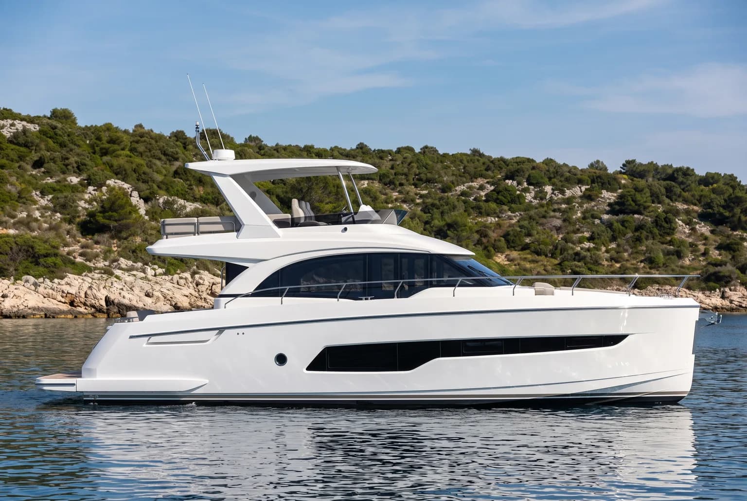 PrimaMare Essential, 12 bis 15 Meter — Seitenansicht bei ruhigem Wasser vor einer bewaldeten Insel.